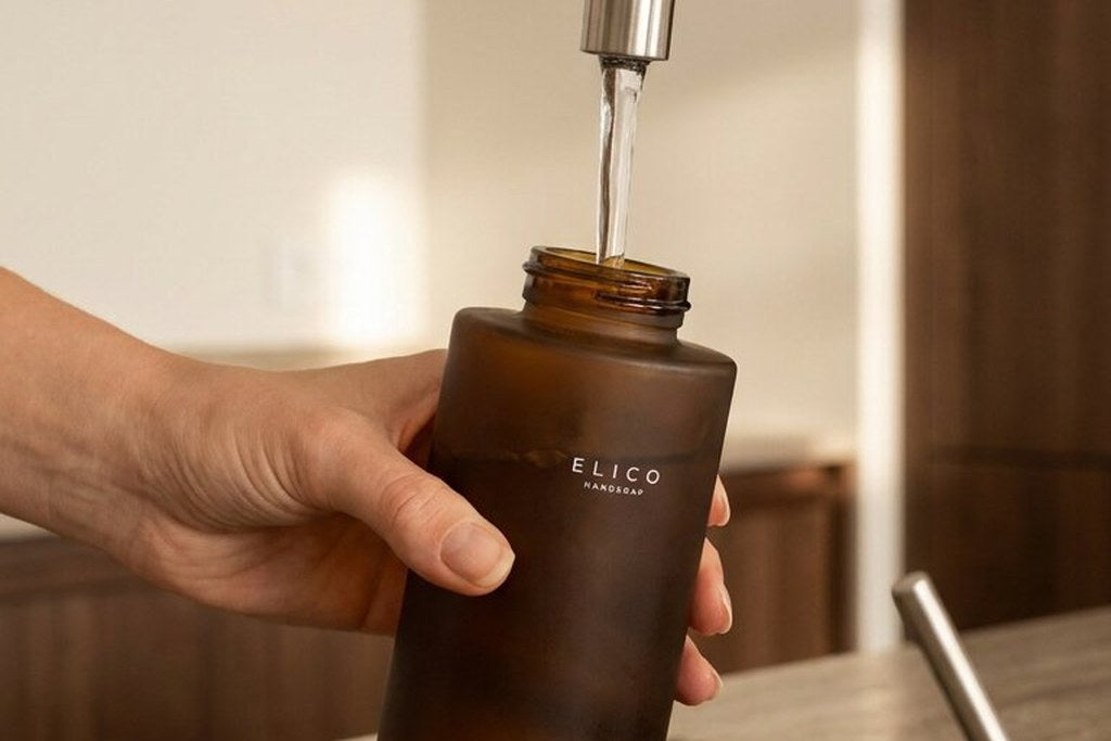 Een hand vult een amberkleurige fles met kraanwater